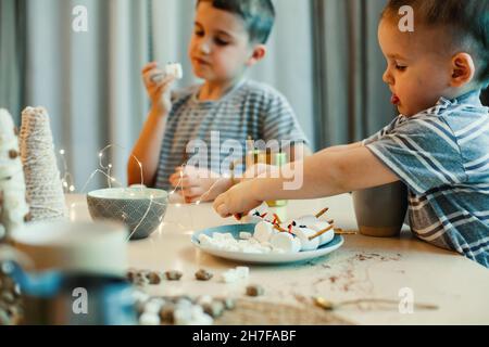 Kinder machen Schneemänner aus Salmhalchen und gesalzenen Trinkhalmen, trinken Kakao in der heimischen Küche. Vorbereitung auf Weihnachten und Neujahr. Stockfoto