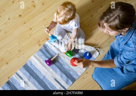 Junge Mutter und kleines Kleinkind spielen kindisch bunte Handglocken Musik zu Hause Stockfoto