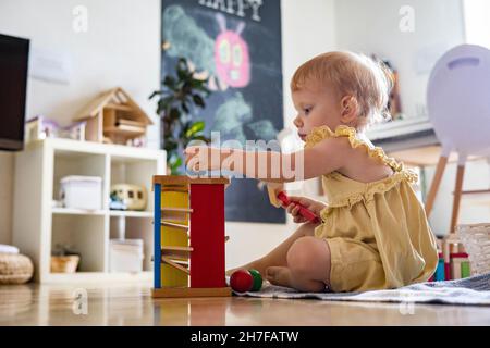 Happy girl Kleinkind Schlagen Holzhammer auf farbigen Kugeln frühe Entwicklung ökologischen Spielzeug Stockfoto