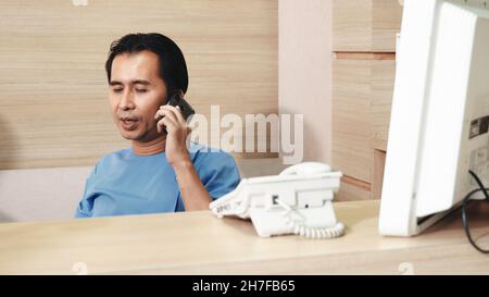 Krankenschwester Mann sitzt in der Theke Bar Büro anrufen Smartphone Gespräch mit dem Patienten, Krankenschwester telefoniert mit Familie während einer Pause im Krankenhaus, Medi Stockfoto