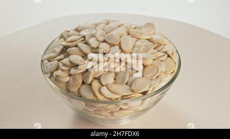 Muttern ungeschälte Kürbiskerne drehen sind auf eine Tabelle in einer Platte. Snack in durchsichtigen Teller auf einem isolierten weißen Hintergrund drehen sich bewegt. Lecker Stockfoto