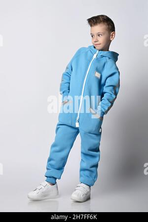 Kid Boy in blauem Jumpsuit mit Kapuze geht mit Händen in Taschen mit reflektierenden Streifen und blickt zur Seite auf den Kopierraum Stockfoto