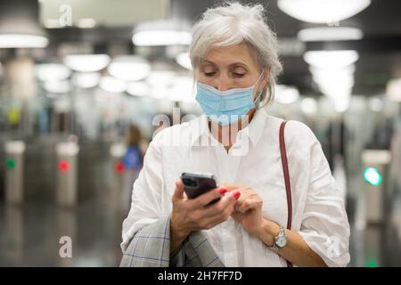Ältere Frau in Maske, die ihr Telefon am Eingang zur U-Bahn-Station benutzte Stockfoto