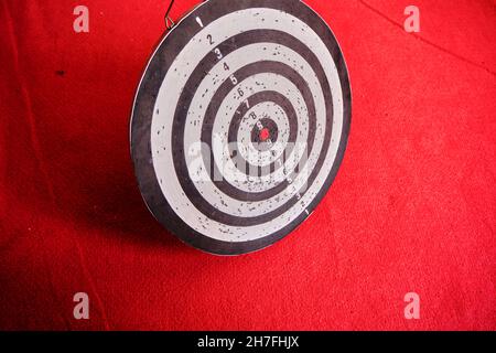 Gebrauchte Dartscheibe, die auf rotem Teppich und seinen Schatten steht. Stockfoto
