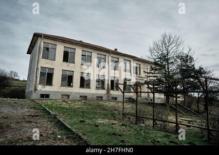 Bulgarien, Kardzali. Altes Brachfeld und verlassene sowjetische Schule mit bewölktem und sehr bewölktem Himmel. Stockfoto