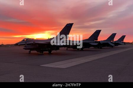 Die Sonne geht über vier F-16-Kampffalken auf, die dem 148th Fighter Wing, Minnesota Air National Guard, zugewiesen wurden. Die 148th führten eine Übung „Agile Combat Employment, ACE“ vom 17. Bis 19. November 2021 durch. ACE ist ein Konzept, das es Fluggeräten ermöglicht, schnell Personal und Jets in entfernten oder heruntergekommenen Umgebungen mit einem viel kleineren Plan bereitzustellen. Piloten, Wartungspersonal für Flugzeuge, Kraftstoffe, Kommunikationspersonal und Sicherheitskräfte simulierten einen Einsatz auf einem abgelegenen Flugplatz mit begrenzter Infrastruktur. Airmen errichteten neue Arbeitsplätze und Infrastruktur mit begrenzter Ausrüstung a Stockfoto