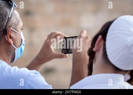 jerusalem-israel. 23-09-2021. Ein Mann mit einer blauen chirurgischen Gesichtsmaske zum Schutz vor dem Corona-Virus nutzt sein Mobiltelefon, um den Western zu fotografieren Stockfoto