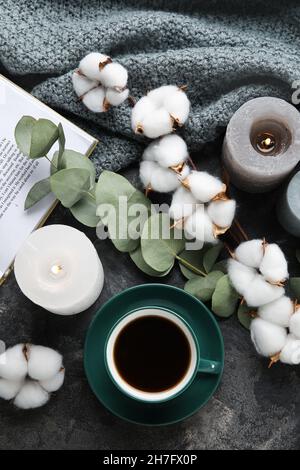 Tasse Kaffee, brennende Kerzen, Buch, Baumwollblumen und Stoff auf dunklem Hintergrund Stockfoto