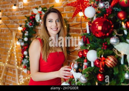 Schönes Mädchen in rotem Kleid feiert Weihnachten. Weihnachtsbaum, Geschenke. Dekoration zum neuen Jahr Stockfoto