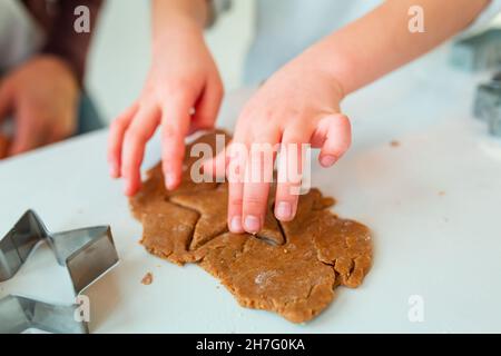 Kinderhände, die Lebkuchen herstellen, Kekse aus Lebkuchenteig schneiden. Weihnachtsbäckerei. Freunde machen Lebkuchen Blick von oben. Festliche Speisen, kochen Stockfoto