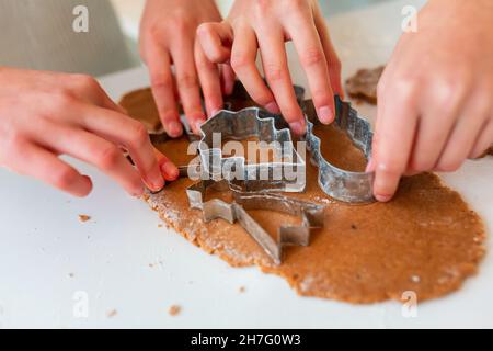 Kinderhände, die Lebkuchen herstellen, Kekse aus Lebkuchenteig schneiden. Weihnachtsbäckerei. Freunde machen Lebkuchen Blick von oben. Festliche Speisen, kochen Stockfoto