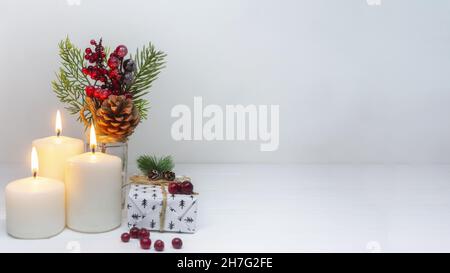 Weihnachtspanorama. Drei Kerzen, eine Schachtel mit einem Weihnachtsgeschenk vom Weihnachtsmann und eine Kiefer mit einem Kegel. Tolle Weihnachtskarte. Stockfoto