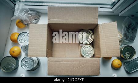 Auspacken Karton Schachtel mit Spenden mit Produkten: Konserven, Getreide, Zitrusfrüchte. Konzept der Nahrungsmittellieferung während der Coronavirus-Pandemie. Stockfoto