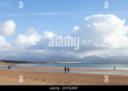 Menschen, die am Strand von Newborough mit den Snowdonia-Bergen im Hintergrund spazieren, Anglesey, Nordwales Stockfoto