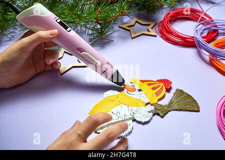 Ein Mädchen zeichnet einen Schneemann mit einem 3d-Stift auf einem violetten Hintergrund Stockfoto