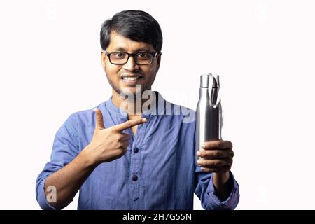 Ein indischer Mann mittleren Alters, der auf eine Edelstahlflasche in der Hand auf weißem Hintergrund zeigt Stockfoto