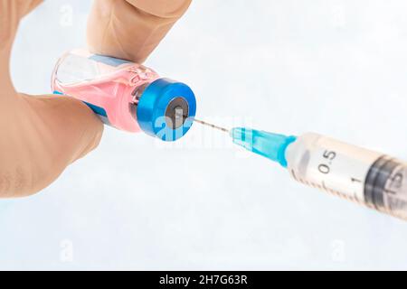 Eine Flasche Impfstoff Nahaufnahme in der Hand eines Arztes mit weißen Handschuhen auf blauem Hintergrund. Stockfoto