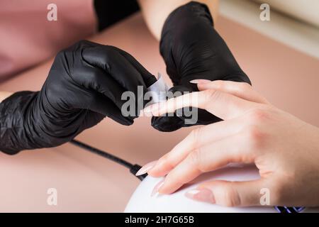 Der Manikurist behandelt den Nagel des Kunden mit einer entfettenden Flüssigkeit, um die Nägel für die Maniküre vorzubereiten und die klebrige Schicht zu entfernen. Stockfoto