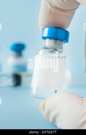 Medizinische Impfstofffläschchen oder -Flaschen auf der Tischplatte auf blauem Hintergrund. Leere Behälterschablone für Etikett. Impfung der Bevölkerung gegen Coronavirus c Stockfoto