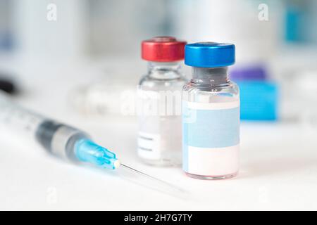 Unbeschriftetes medizinisches Glasfläschchen und Kunststoffspritze zur Injektion auf weißem Tisch mit blauem Hintergrund. Konzept der Impfung, Diabetes, cosme Stockfoto