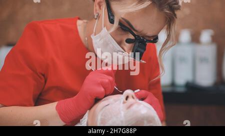 Quetschen von Akne von einem Mädchen mit problematischen Haut im Salon mit einer Schleife. Stockfoto