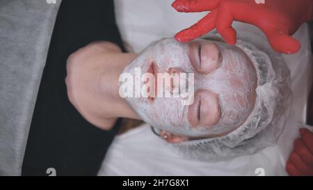 Anwendung einer Creme-Maske auf das Gesicht eines Mädchens mit Problemhaut im Salon. Stockfoto