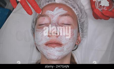 Anwendung einer Creme-Maske auf das Gesicht eines Mädchens mit Problemhaut im Salon. Stockfoto