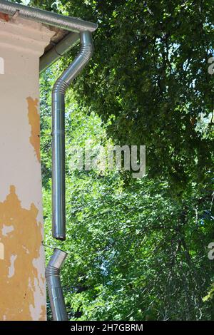 Nahaufnahme einer zerbrochenen Dachrinne aus Metall, beschädigtes Fallrohr, Abfluss eines alten Hauses, das renoviert werden muss, Dachrinne muss repariert werden. Stockfoto