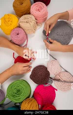 Draufsicht auf weibliche Hände mit Stricken auf einem weißen Tisch. Zwei Frauen stricken Körbe aus Baumwollgarn. Stockfoto
