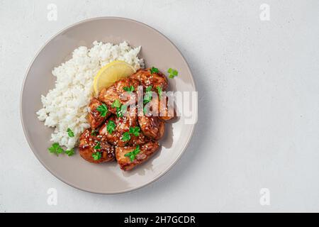 Teriyaki-Huhn mit Reis und Sesam auf einem beigen Teller auf grauem Hintergrund. Stockfoto