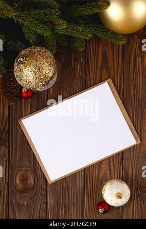 Weihnachtskarte Mockup. Weiße, minimale leere Postkarte auf Holztisch mit festlichen Dekorationen und Bastelumschlag. Stockfoto