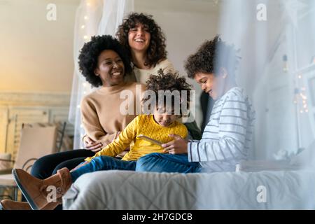 Glückliche multiethnische Familie. Lächelnde schwule Frauen verbringen zu Hause Zeit mit Kindern. Stockfoto