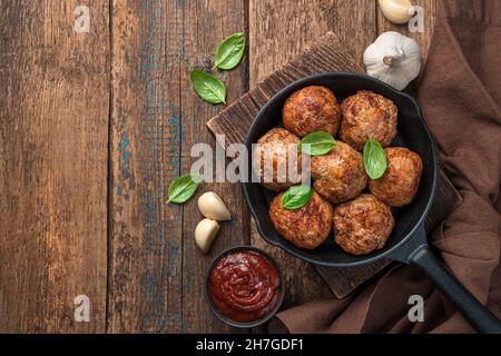 Fleischbällchen mit frischem Basilikum in einer Pfanne auf Holzboden. Stockfoto