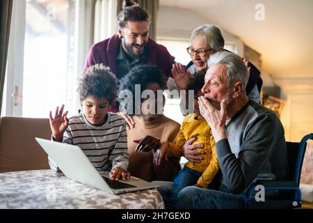 Fröhliche, mehrfache Familie, die sich um Notebbok versammelt und sich während eines Videoanrufs amüsieren kann Stockfoto