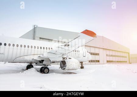 Weißes Passagierflugzeug in der Nähe des Flugzeughangars bei kaltem Winterwetter. Das Flugzeug muss repariert werden Stockfoto