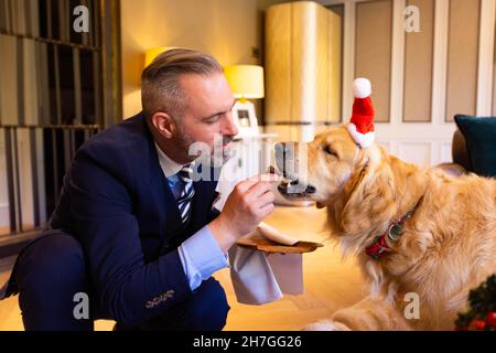 NUR FÜR REDAKTIONELLE VERWENDUNG Butler Lucas Kongiel hilft Golden Retriever Boris bei der Kostprobe von Hiltons neuem festlichen Menü für Hunde im Biltmore Mayfair, LXR Hotels & Resorts, London. Ausgabedatum: Dienstag, 23. November 2021. Stockfoto