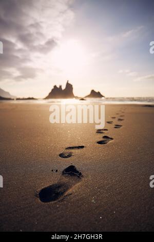 Fußabdrücke im Sand am Strand, der zum Meer führt. Goldener Sonnenuntergang auf Teneriffa, Kanarische Inseln, Spanien. Stockfoto