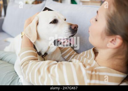 Porträt einer jungen Frau, die mit Hund kuschelt, während sie zu Hause auf der Couch liegt, Raum kopieren Stockfoto