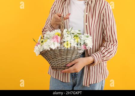 Mädchen hält Korb mit Blumen auf gelbem Hintergrund Stockfoto