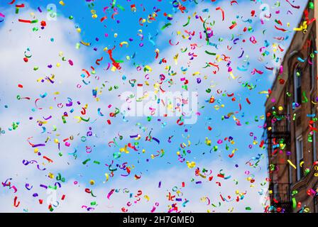 Niedriger Blickwinkel auf einen weiß getrübten blauen Himmel, gefüllt mit bunten Konfetti oder Streamern während einer Straßenparade, bei der das Gebäude im Hintergrund außer Fokus steht Stockfoto