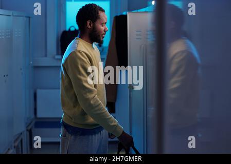 Junger Sportler in Sweatshirt und Sweathose, der vor einer Reihe von Schließfächern in einer kleinen Umkleidekabinen steht Stockfoto