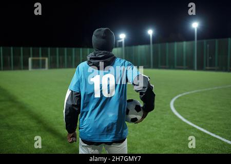 Rückansicht eines modernen Profifußballspielers mit Ball, der vor einem großen Fußballfeld steht Stockfoto