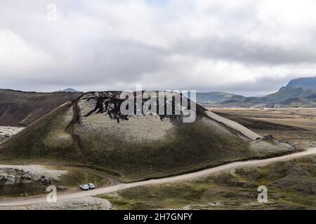 Blick aus der Höhe auf einen schlafenden Vulkan auf dem Vulkanplateau in der Nähe des Katla Vulkans in Island mit Bergen im Hintergrund und Autos geparkt Stockfoto