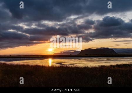 Panoramablick entlang der Küste Islands bei spätem Sonnenuntergang mit großen Felsformationen im Meer und dunklen Wolken am Himmel Stockfoto
