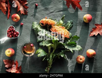 Orangefarbene Chrysanthemenblüten, trockenes Hasenschwanzgras und rote Eichenblätter, Kürbisse, Cranberry. Herbstschmuck, flach auf dunklem Textil. Stockfoto