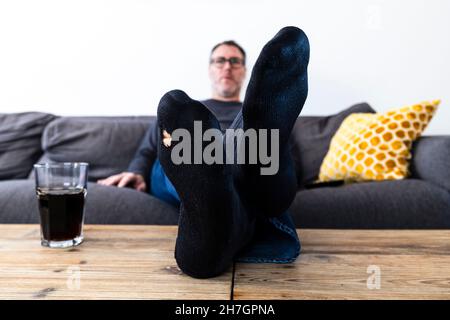 Mann mit einem Loch in seiner Socke, der auf der Couch sitzt Stockfoto