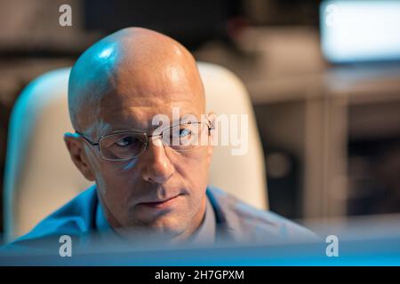 Erfahrener Geschäftsmann in einer Brille, der Daten auf dem Computerbildschirm ansieht, während er an seinem Arbeitsplatz im Büro sitzt Stockfoto