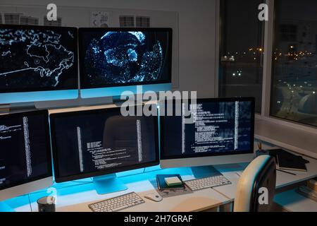 Teil des großen Openspace-Büro der Programmierfirma mit langem Schreibtisch und mehreren Computermonitoren mit kodierten Daten Stockfoto