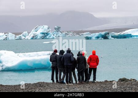 Gruppe von Menschen, die die Lagune vor dem Solheimajokull Gletscher in Island mit einem großen Stück Gletschereis im Wasser beobachten Stockfoto