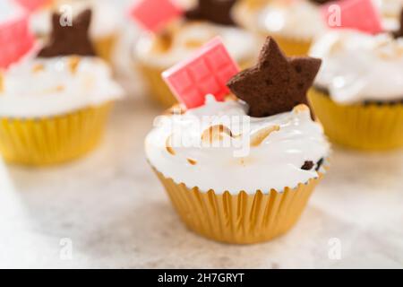 Gourmet-S'mores-Cupcakes mit Meringue-Zuckerguss und garniert mit sternförmiger Schokolade graham Cracker und einer pinken Mini-Tafel Schokolade. Stockfoto